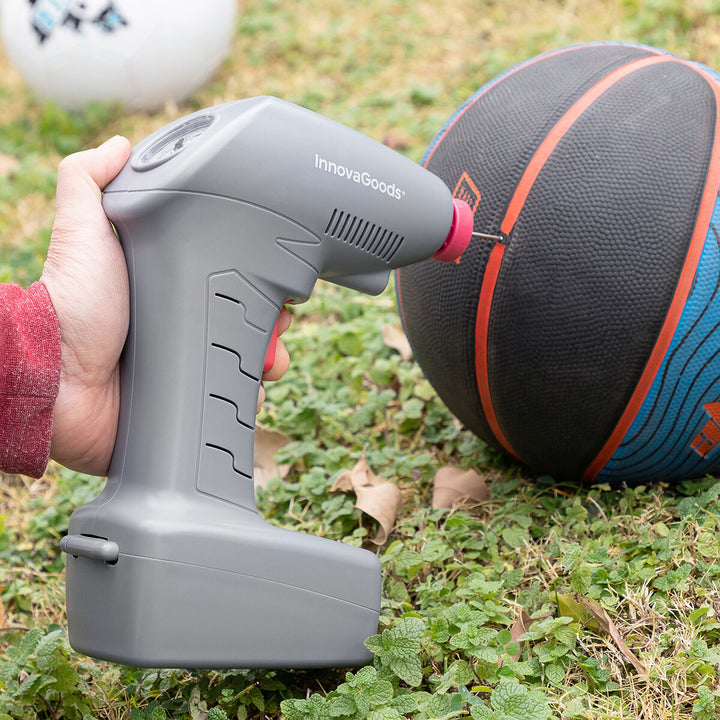 Grauer, tragbarer Luftkompressor Airpro+ von InnovaGoods pumpt einen Basketball auf.