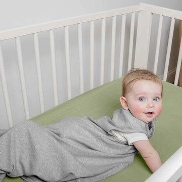 Baby trägt grauen Ingenuity Schlafsack im weißen Kinderbett. Bequemes Material für Babys.