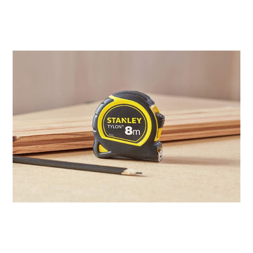 Gelb-schwarzes Stanley Flexometer 8m auf Holz mit Bleistift. Präzises Messwerkzeug.