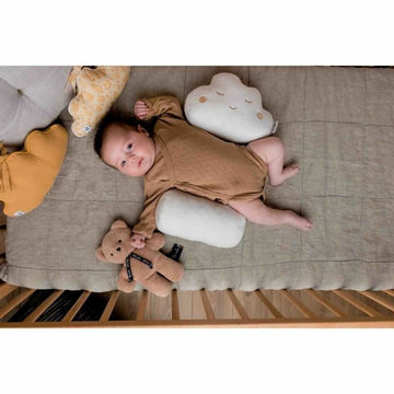 Weißes Tineo Cloudy Kissen in Wolkenform mit Gesicht neben Baby auf gesteppter Decke.