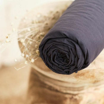 Gerolltes Anthrazit Spannbetttuch 140x190 cm mit glatter Textur und floralen Akzenten.