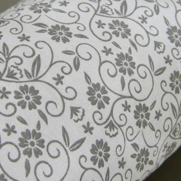 Nahaufnahme des Kissens mit grauem Blumenmuster und Ranken auf weißem Stoff.