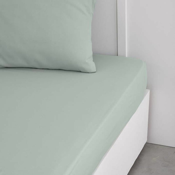Hellgrünes Spannbetttuch (160x200) aus der TODAY Essential Kollektion auf einem Bett mit Kissen.