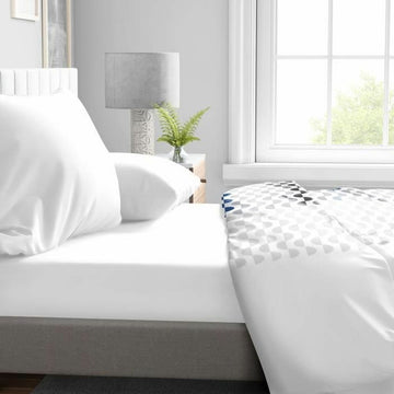 Weißes Spannbetttuch 90x190 cm auf einem Bett. Glatte, straffe Passform.