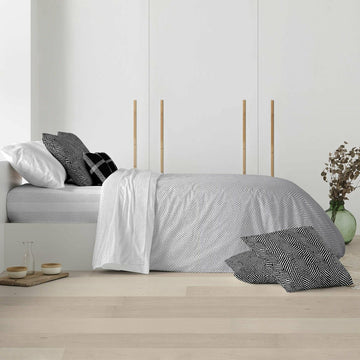 Bett mit hellgrauem Zickzack-Bettdeckenbezug und geometrischen Kissenbezügen.