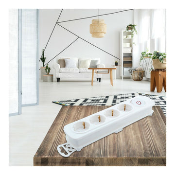 Weiße Steckdosenleiste mit vier Steckdosen und Schalter auf einem Holztisch im Wohnzimmer.