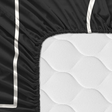 Detailaufnahme: Schwarzes HappyFriday Bettlaken mit weißem Streifen auf Matratze.