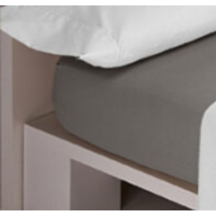 Graues Spannbetttuch LISOS COTTON auf einem Bett mit einem weißen Kissen im Hintergrund.