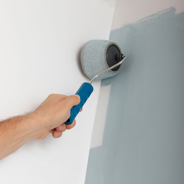 Wiederbefüllbarer Farbroller mit blauem Griff streicht Wand. Anti-Tropf Design für gleichmäßigen Farbauftrag.