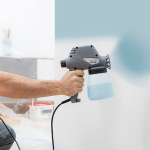 Graue elektrische Farbspritzpistole Spraint+ im Einsatz, sprüht Farbe auf weiße Wand.