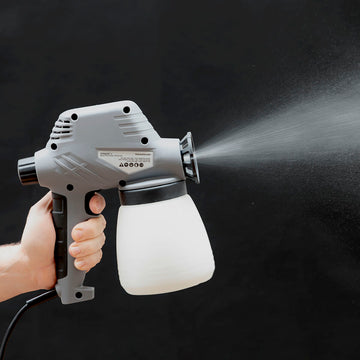 Graue elektrische Farbspritzpistole Spraint+ von InnovaGoods beim Sprühen vor schwarzem Hintergrund.