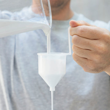 Weisse Farbe wird in den Trichter der elektrischen Farbspritzpistole gegossen.