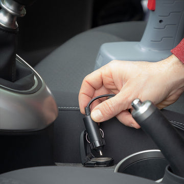 Schwarzer, tragbarer Luftkompressor wird an Zigarettenanzünder im Auto angeschlossen.