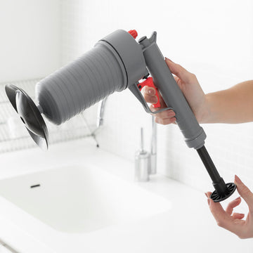 Graue KlinGun InnovaGoods Abflussreinigungs-Pistole mit Adaptern über einem Waschbecken.