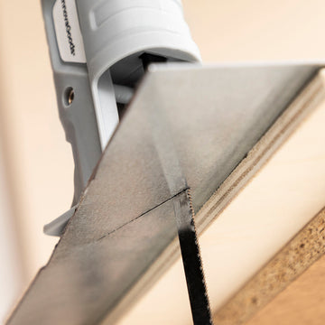 Grauer Stichsägen-Adapter schneidet Holz. Praktisches Zubehör für Bohrmaschinen.